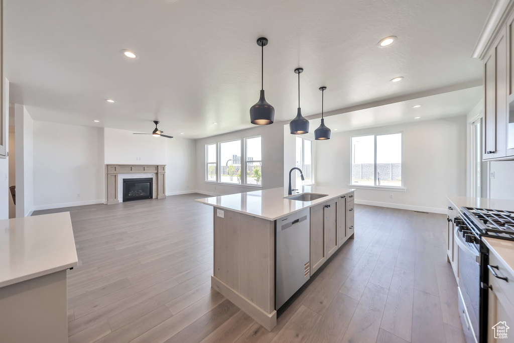 Kitchen with stainless steel appliances, a sink, baseboards, ceiling fan, and light wood-type flooring