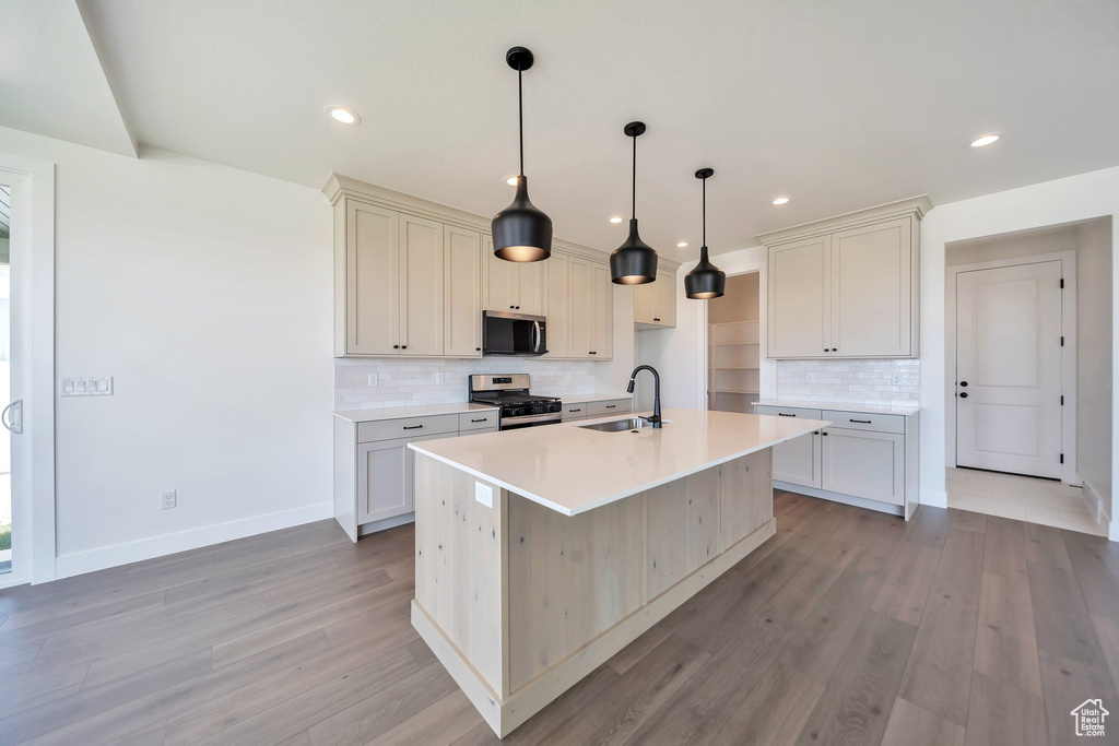 Kitchen featuring stainless steel appliances, a sink, backsplash, a kitchen island with sink, and light wood-type flooring