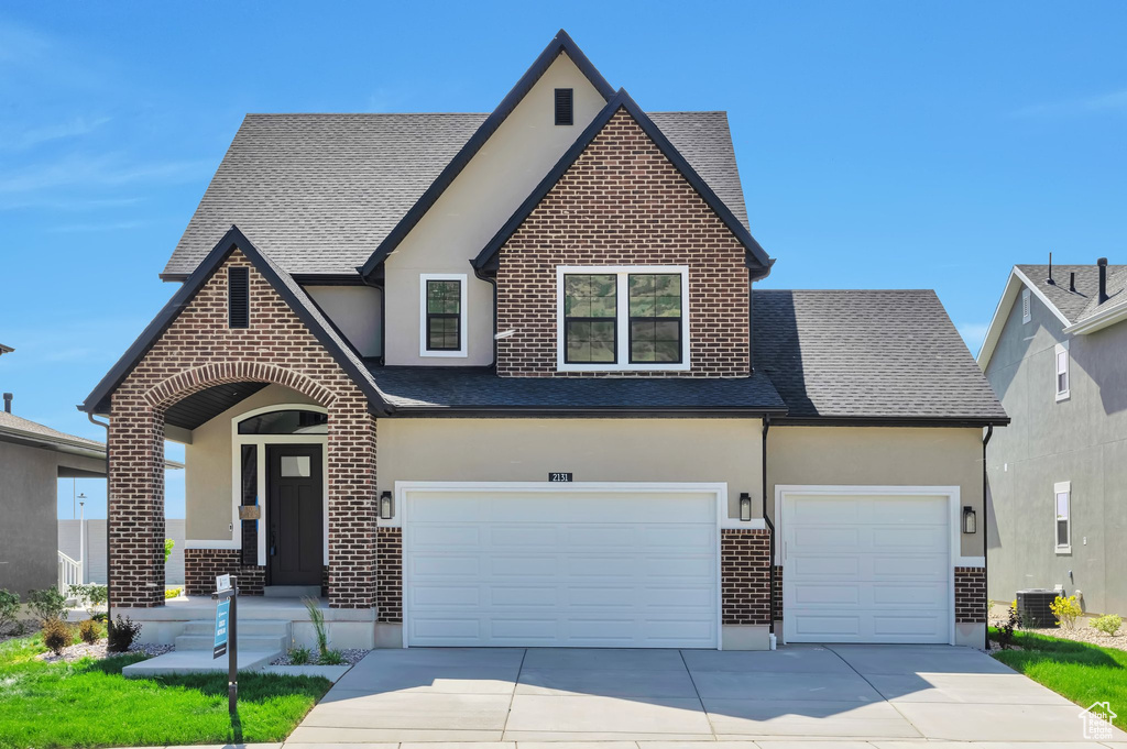 View of front of property featuring stucco siding, driveway, a shingled roof, and brick siding