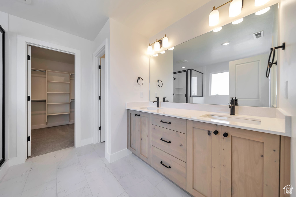 Full bath featuring marble look tile flooring, double vanity, a stall shower, baseboards, and a walk in closet