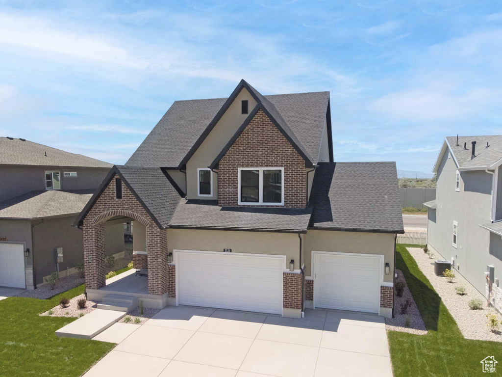 View of front facade featuring brick siding, a shingled roof, driveway, a garage, and stucco siding