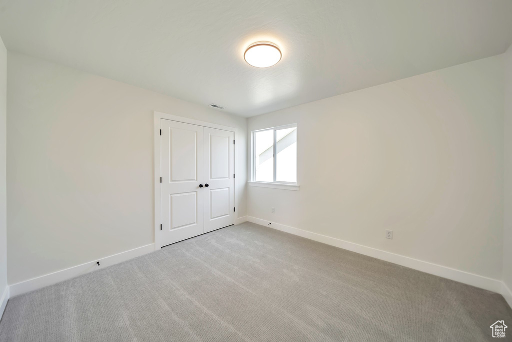 Unfurnished bedroom featuring baseboards, light colored carpet, and a closet