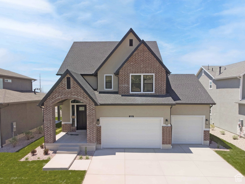 View of front of property with brick siding, stucco siding, roof with shingles, a garage, and driveway