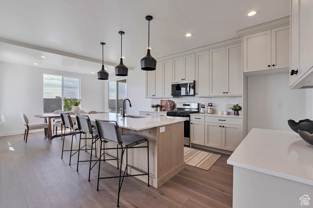 Kitchen with appliances with stainless steel finishes, wood finished floors, backsplash, a kitchen bar, and recessed lighting
