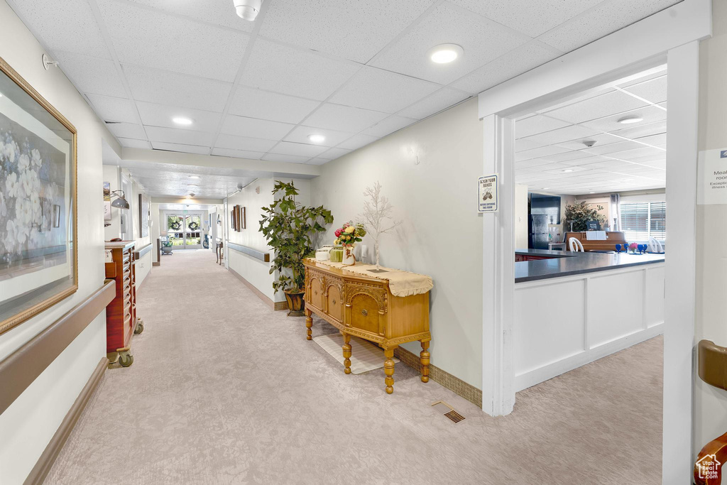 Hallway featuring a drop ceiling, light colored carpet, baseboards, and recessed lighting