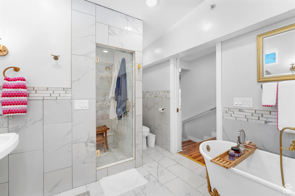 Full bathroom with marble look tile flooring, a shower stall, a freestanding bath, tile walls, and toilet
