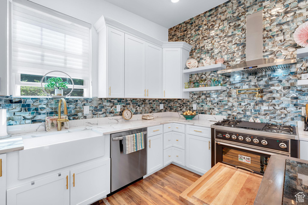 Kitchen featuring appliances with stainless steel finishes, a sink, wall chimney exhaust hood, white cabinets, and light stone counters