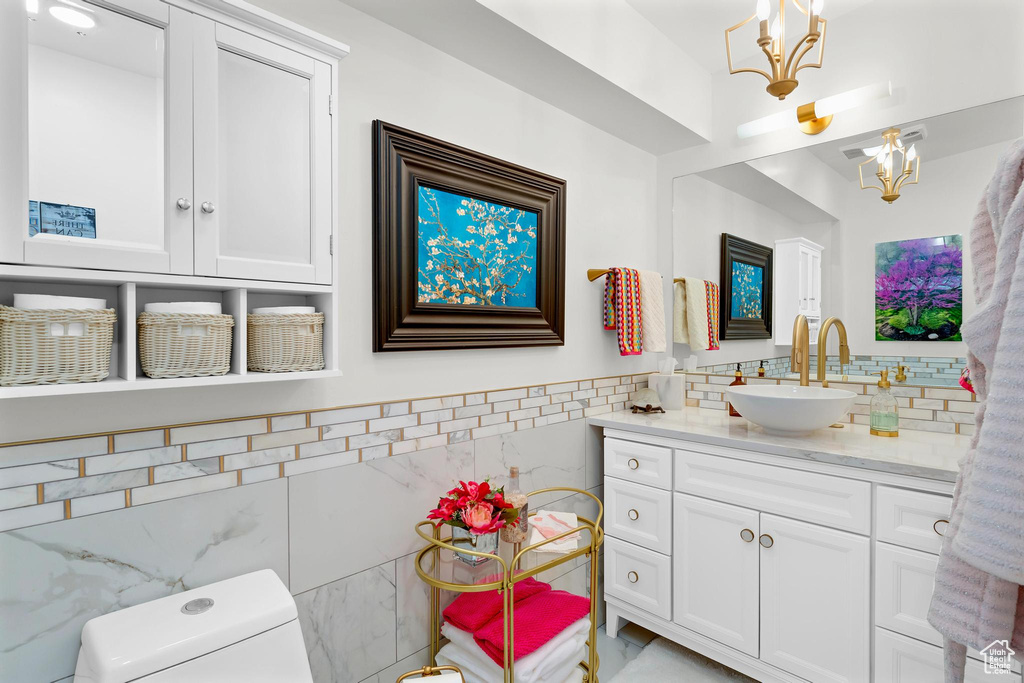 Bathroom featuring tile walls, toilet, a chandelier, vanity, and a wainscoted wall
