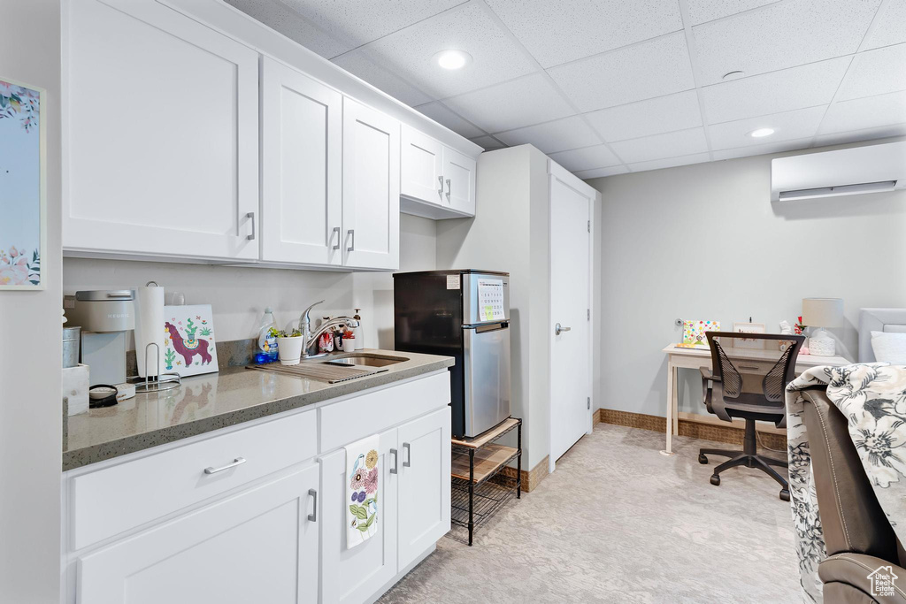 Kitchen with a wall mounted air conditioner, a sink, freestanding refrigerator, dark stone countertops, and white cabinets