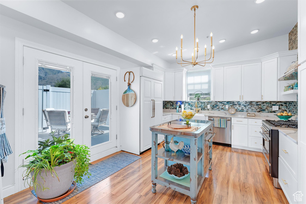 Kitchen featuring premium appliances, light countertops, decorative backsplash, white cabinets, and a chandelier