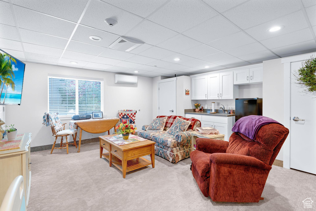 Living room with a wall unit AC, light colored carpet, a paneled ceiling, and baseboards