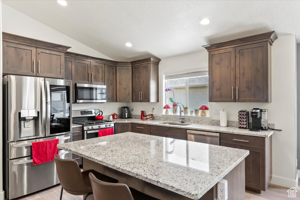 Kitchen featuring appliances with stainless steel finishes, a sink, dark brown cabinets, a center island, and a breakfast bar area