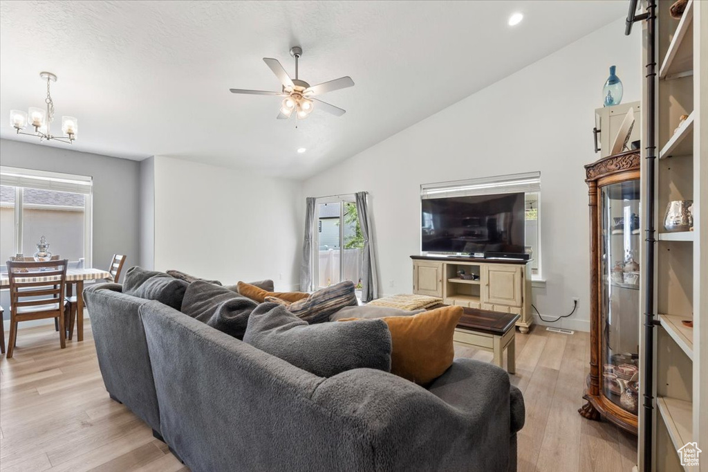 Living area with lofted ceiling, a ceiling fan, light wood-type flooring, healthy amount of natural light, and a chandelier