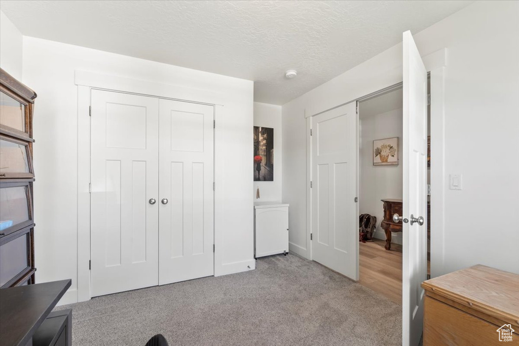 Bedroom with light colored carpet, baseboards, a closet, and a textured ceiling