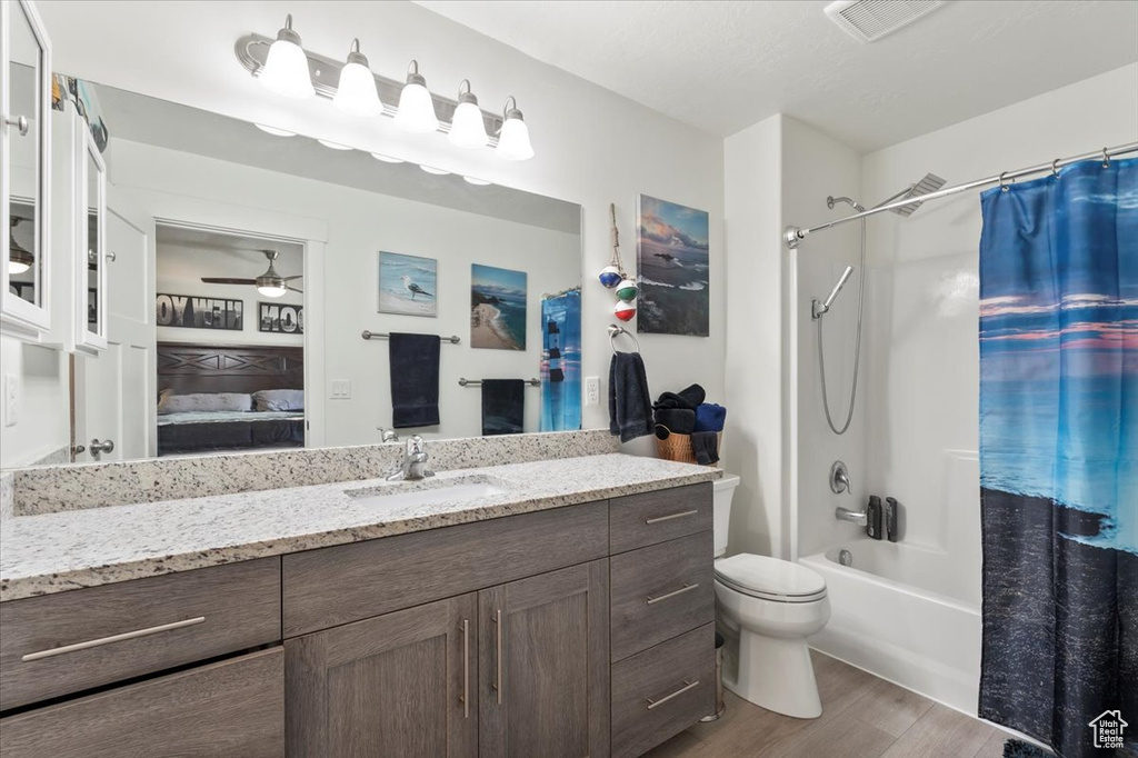 Ensuite bathroom with wood finished floors, a ceiling fan, vanity, shower / bath combination with curtain, and toilet