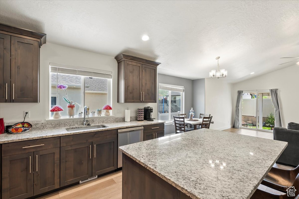 Kitchen featuring a sink, stainless steel dishwasher, a kitchen island, dark brown cabinets, and light stone countertops