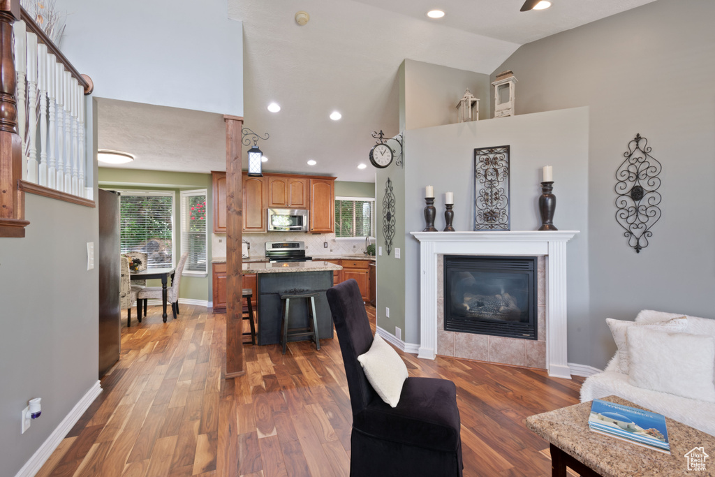 Living area with high vaulted ceiling, wood finished floors, healthy amount of natural light, a glass covered fireplace, and baseboards
