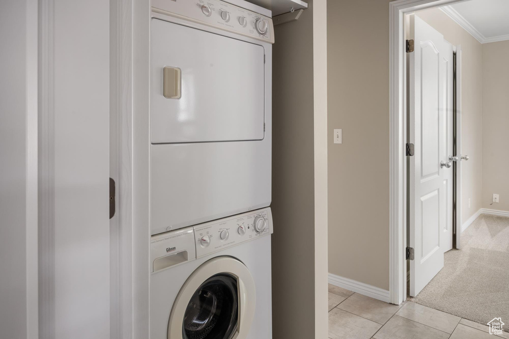 Washroom featuring stacked washer and clothes dryer, ornamental molding, baseboards, light tile patterned floors, and light colored carpet