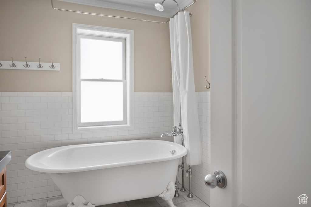 Full bath with tile walls, tile patterned floors, healthy amount of natural light, a freestanding bath, and wainscoting