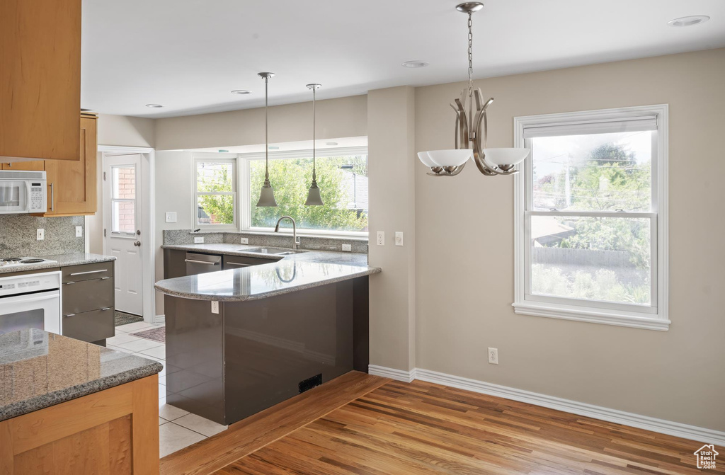 Kitchen featuring white appliances, a sink, tasteful backsplash, light wood finished floors, and hanging light fixtures