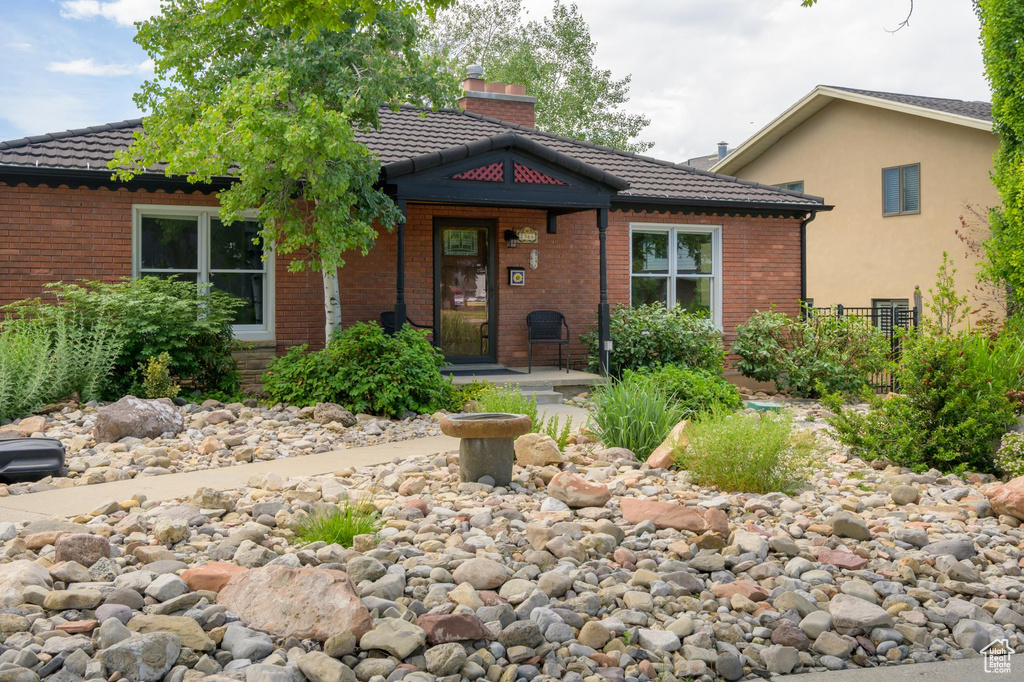 View of front of home featuring brick siding, a chimney, and a tiled roof