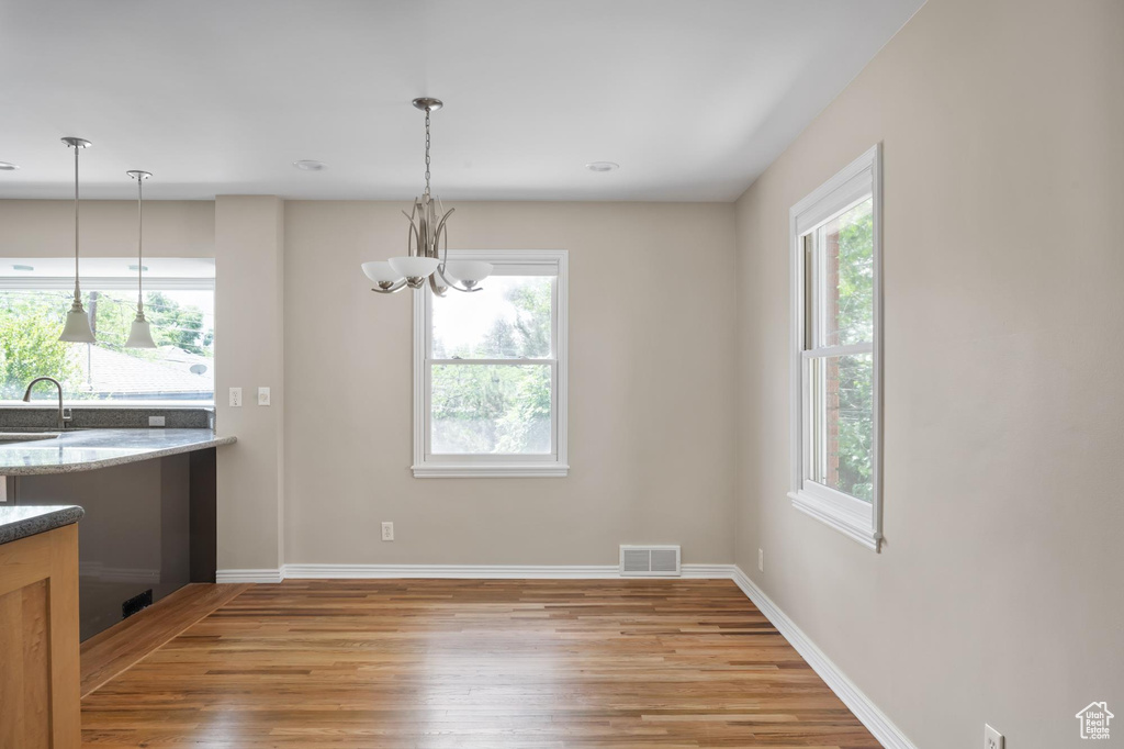 Unfurnished dining area with light wood finished floors, healthy amount of natural light, a sink, and a chandelier