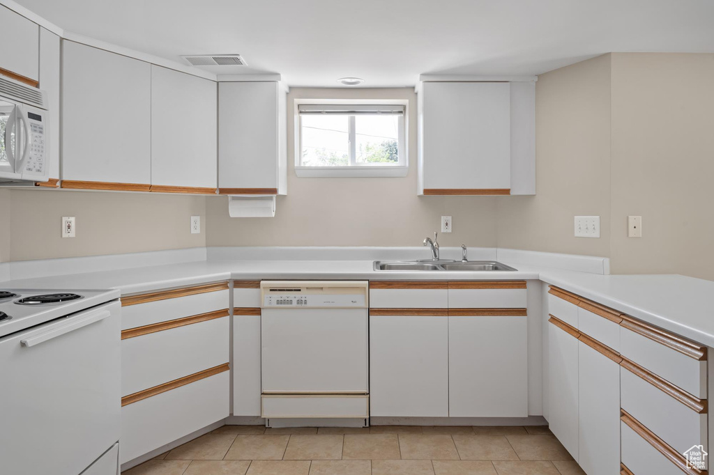 Kitchen with white appliances, a sink, light countertops, white cabinets, and light tile patterned floors