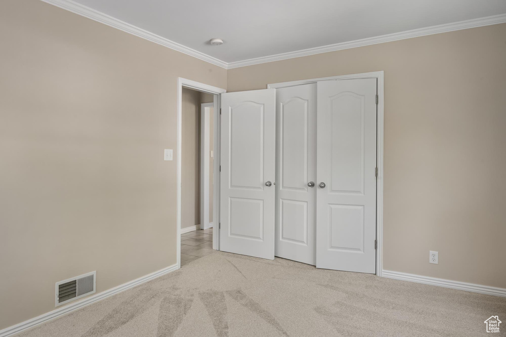 Unfurnished bedroom with light colored carpet, crown molding, baseboards, and a closet