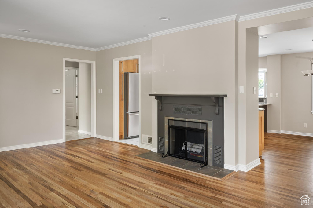 Unfurnished living room featuring light wood-type flooring, ornamental molding, baseboards, a tile fireplace, and recessed lighting