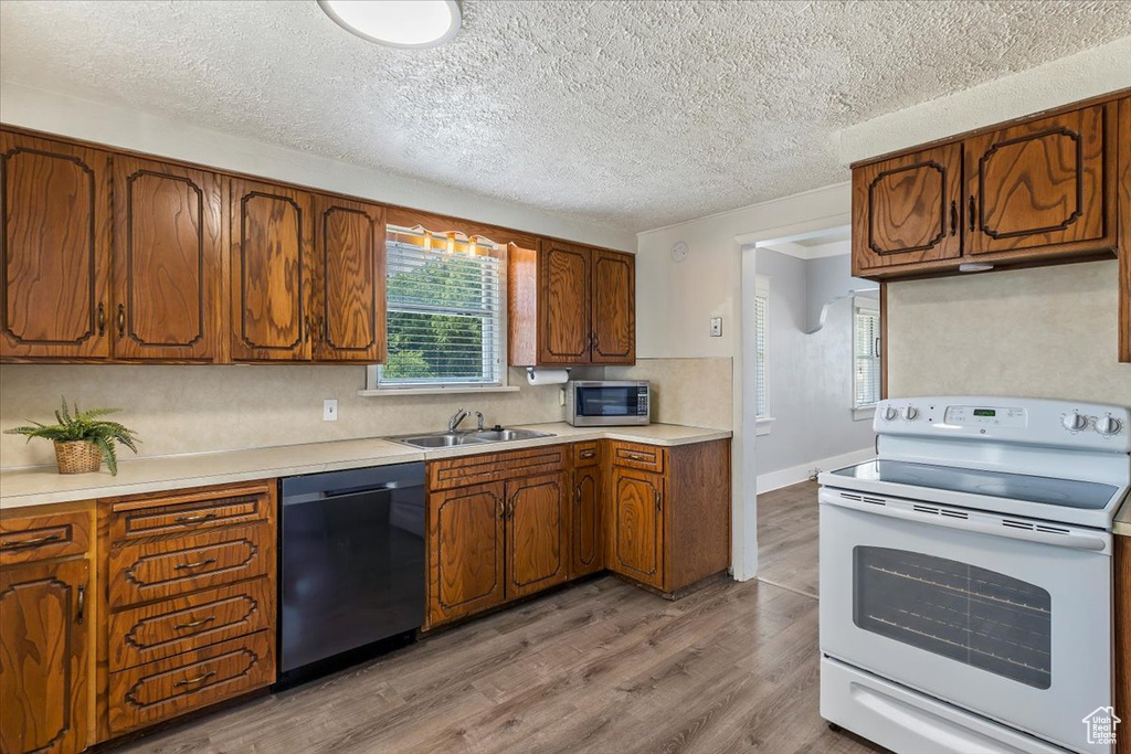 Kitchen featuring appliances with stainless steel finishes, a sink, brown cabinetry, wood finished floors, and a textured ceiling