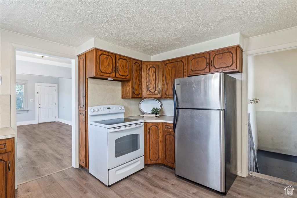 Kitchen with electric stove, freestanding refrigerator, light countertops, brown cabinetry, and a textured ceiling