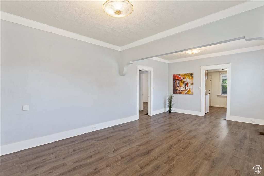 Spare room featuring baseboards, wood finished floors, a textured ceiling, and ornamental molding