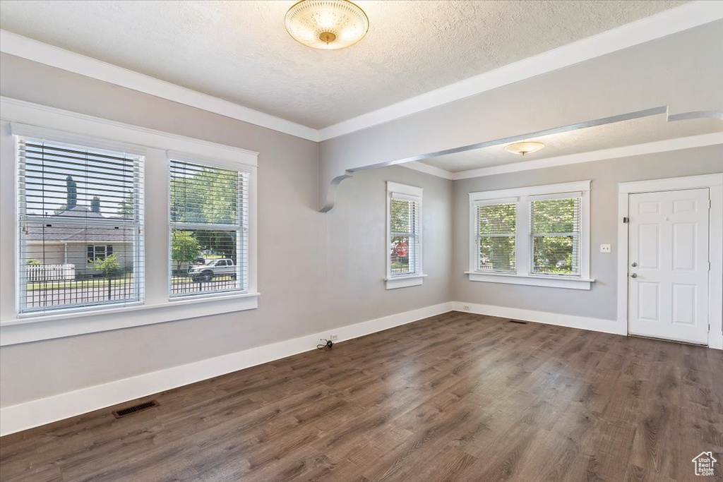 Unfurnished room featuring dark wood finished floors, healthy amount of natural light, baseboards, a textured ceiling, and ornamental molding