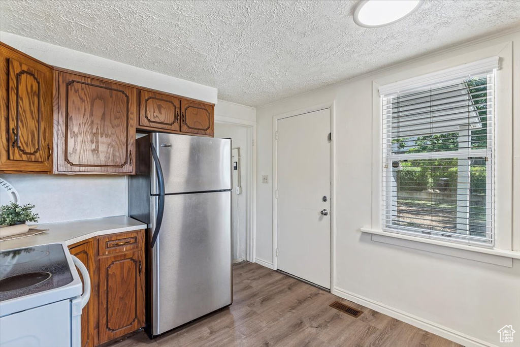 Kitchen featuring freestanding refrigerator, light wood-type flooring, a textured ceiling, brown cabinetry, and light countertops