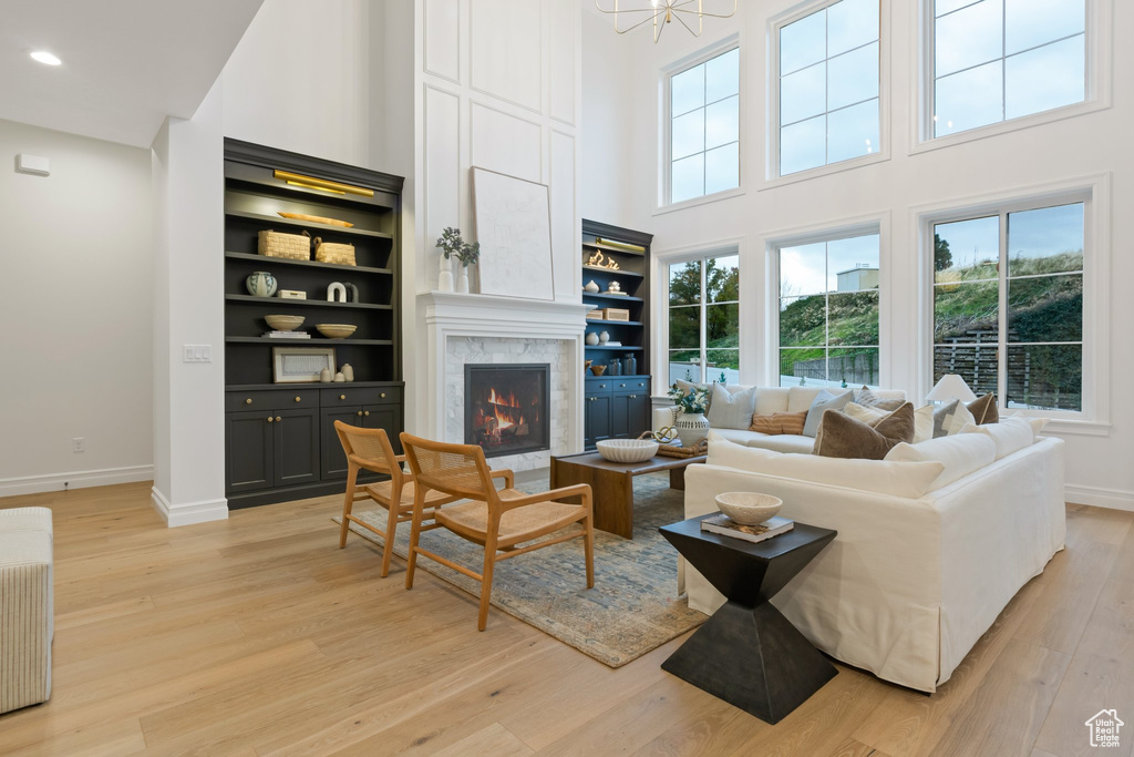 Living area with a high ceiling, a premium fireplace, baseboards, light wood finished floors, and recessed lighting