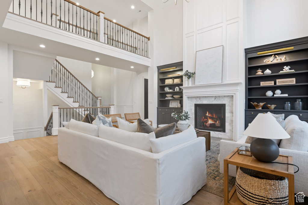 Living area featuring a high ceiling, light wood-style flooring, a lit fireplace, built in shelves, and stairway