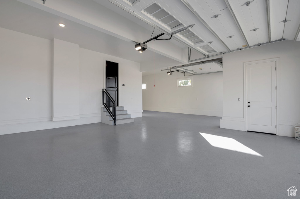 Garage with a garage door opener, recessed lighting, and baseboards