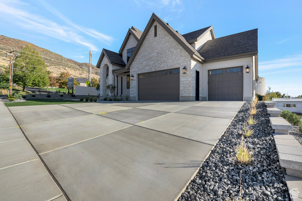 View of front of home with a garage, driveway, stone siding, a mountain view, and a shingled roof