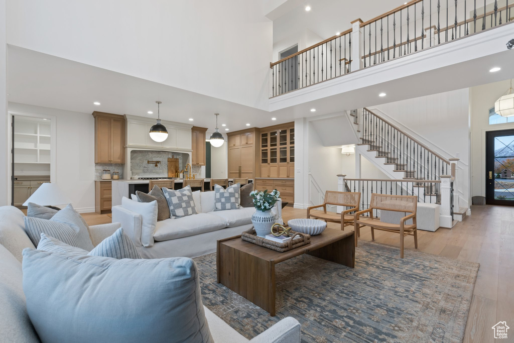 Living room with a high ceiling, light wood-type flooring, stairs, and recessed lighting