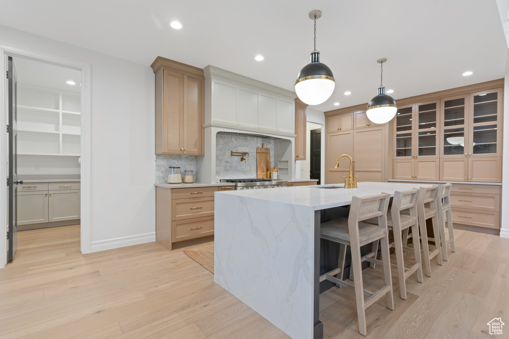 Kitchen featuring a sink, light wood-style floors, recessed lighting, decorative backsplash, and a kitchen island with sink