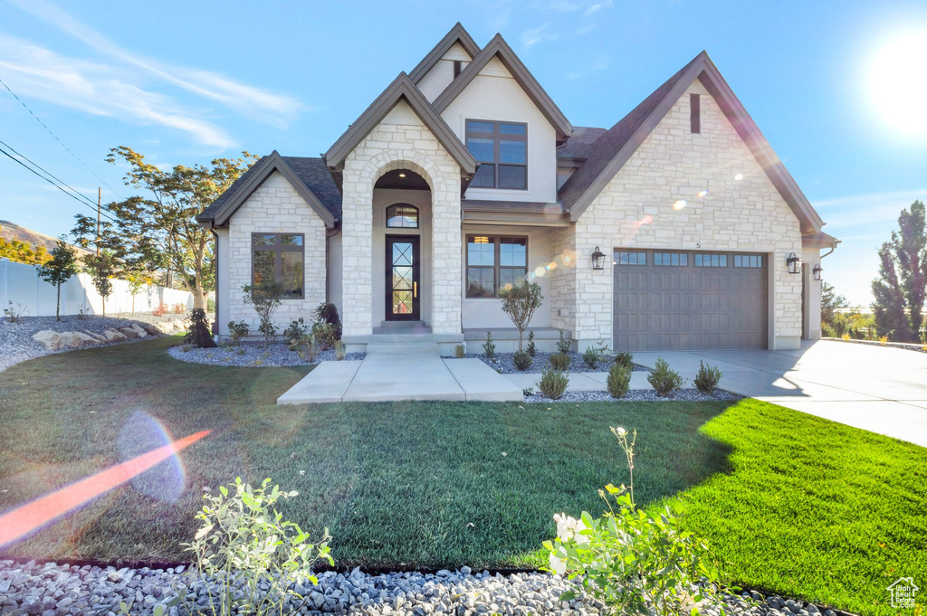 View of front of property with stone siding, driveway, an attached garage, and stucco siding