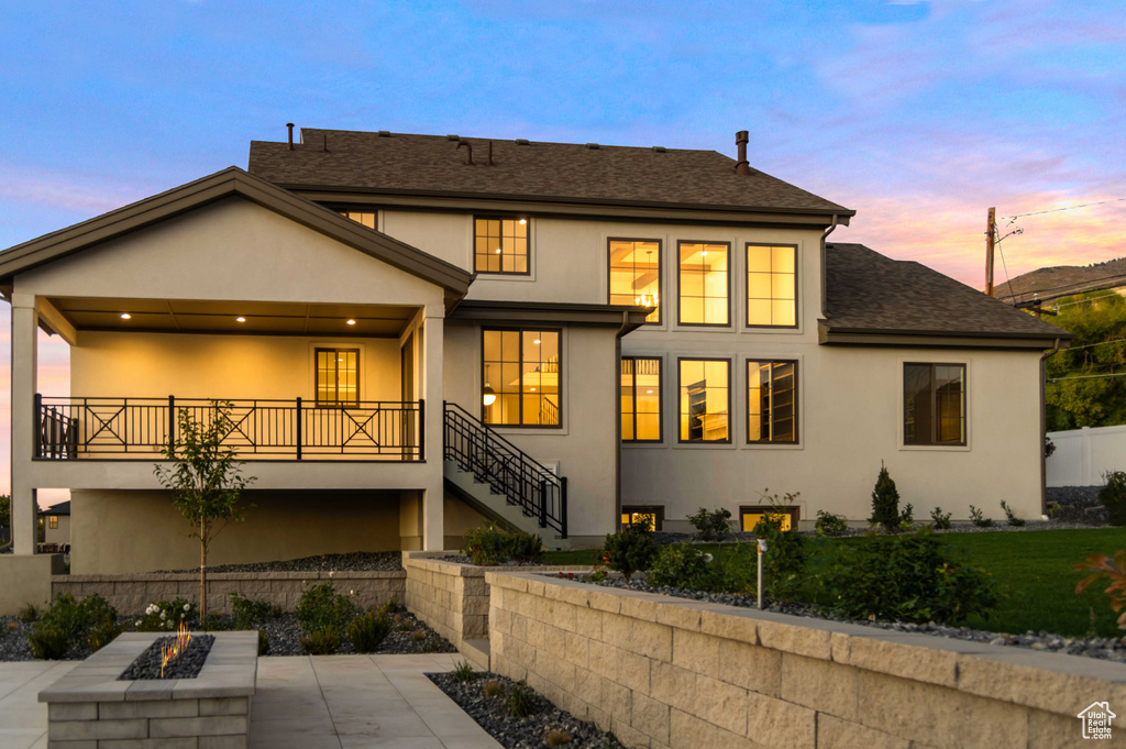 Back of property at dusk featuring an outdoor fire pit, stucco siding, stairs, roof with shingles, and a patio
