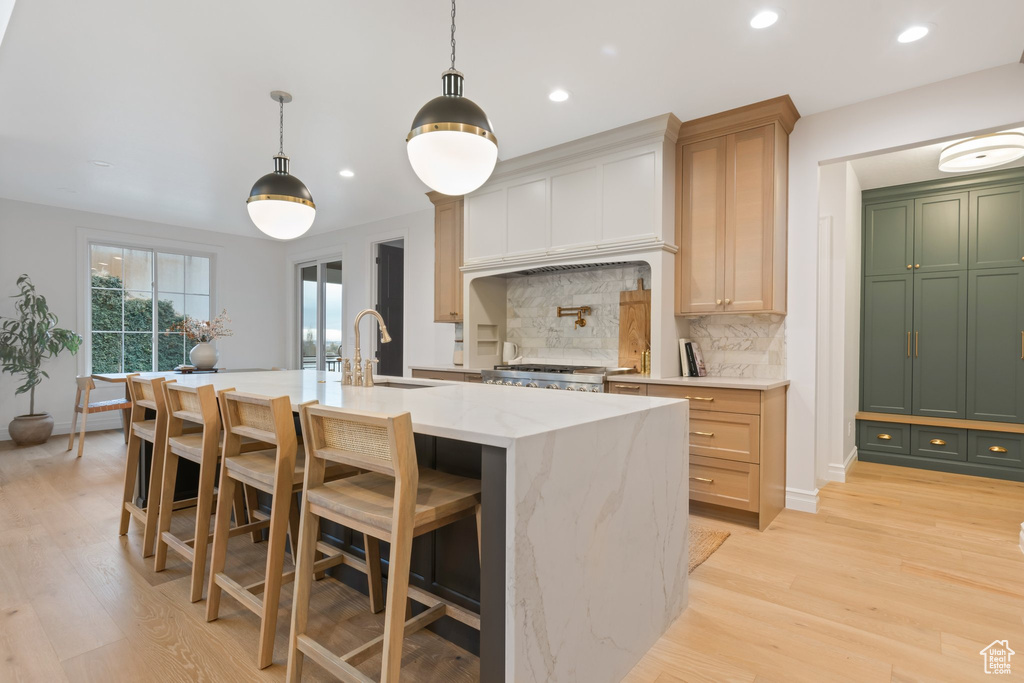 Kitchen featuring a sink, decorative backsplash, light wood-style flooring, an island with sink, and recessed lighting