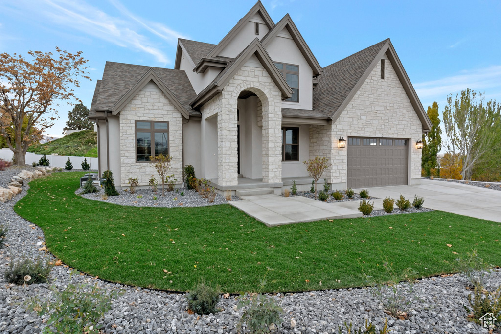 French country style house featuring stone siding, driveway, a shingled roof, stucco siding, and a garage