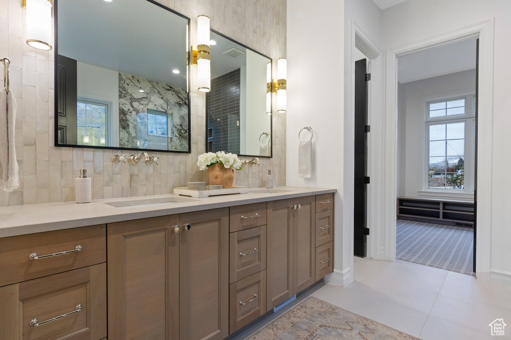 Full bathroom featuring double vanity, backsplash, a tile shower, tile patterned floors, and baseboards