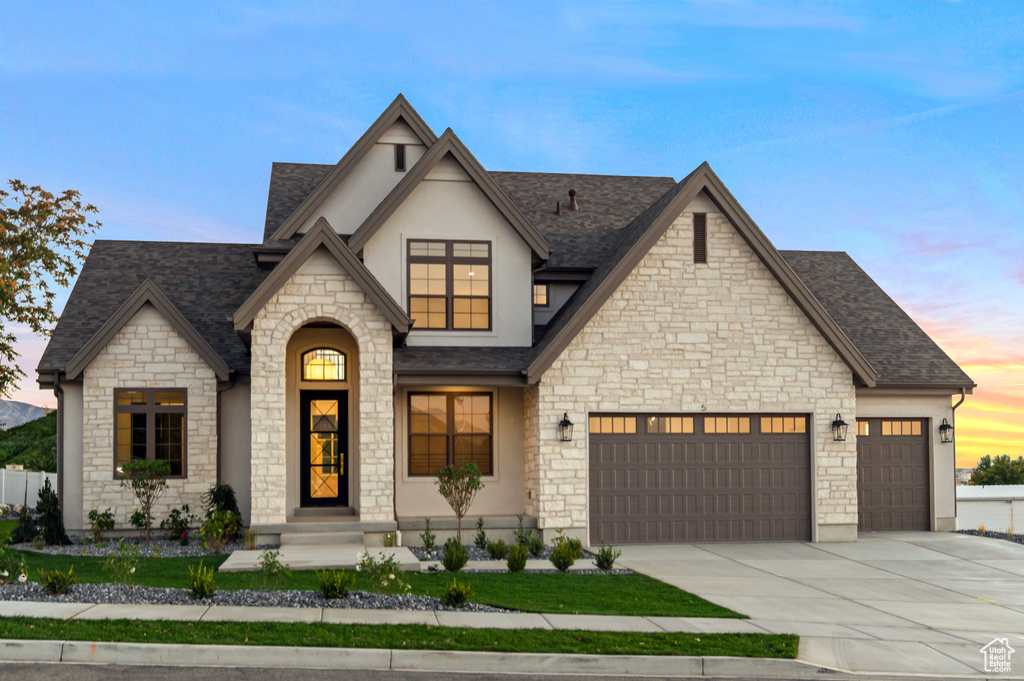 View of front of property with a garage, concrete driveway, a shingled roof, stucco siding, and stone siding