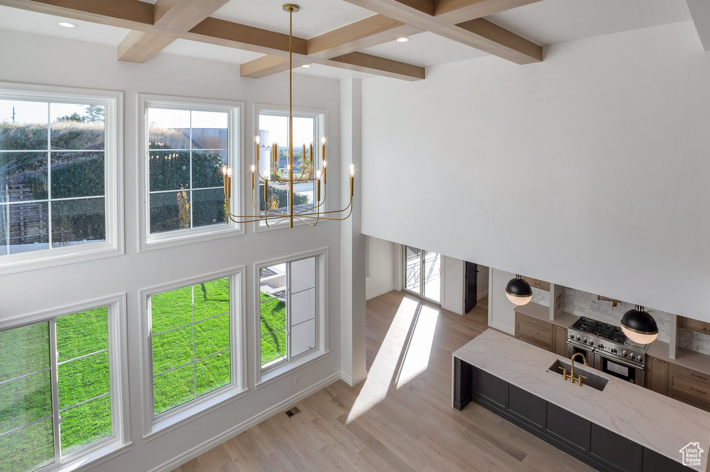 Interior space with coffered ceiling, light wood-type flooring, beam ceiling, baseboards, and a chandelier