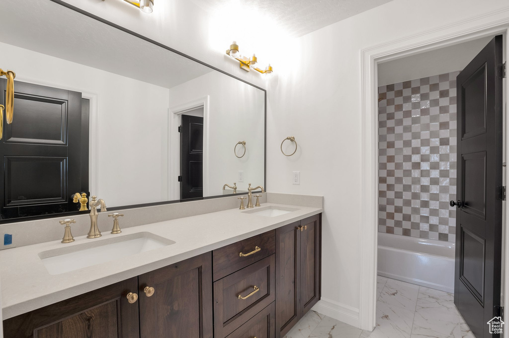 Bathroom featuring marble look tile flooring, double vanity, and baseboards