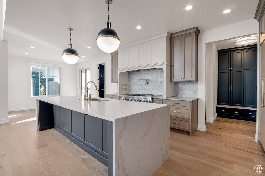 Kitchen featuring a sink, tasteful backsplash, light wood-style flooring, a center island with sink, and recessed lighting