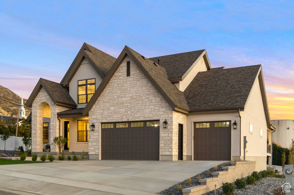 View of front of house featuring a garage, concrete driveway, stone siding, and roof with shingles
